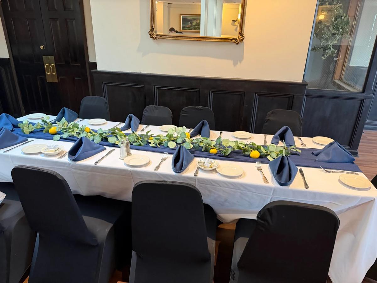 A long party table with greenery, lemons and navy napkins