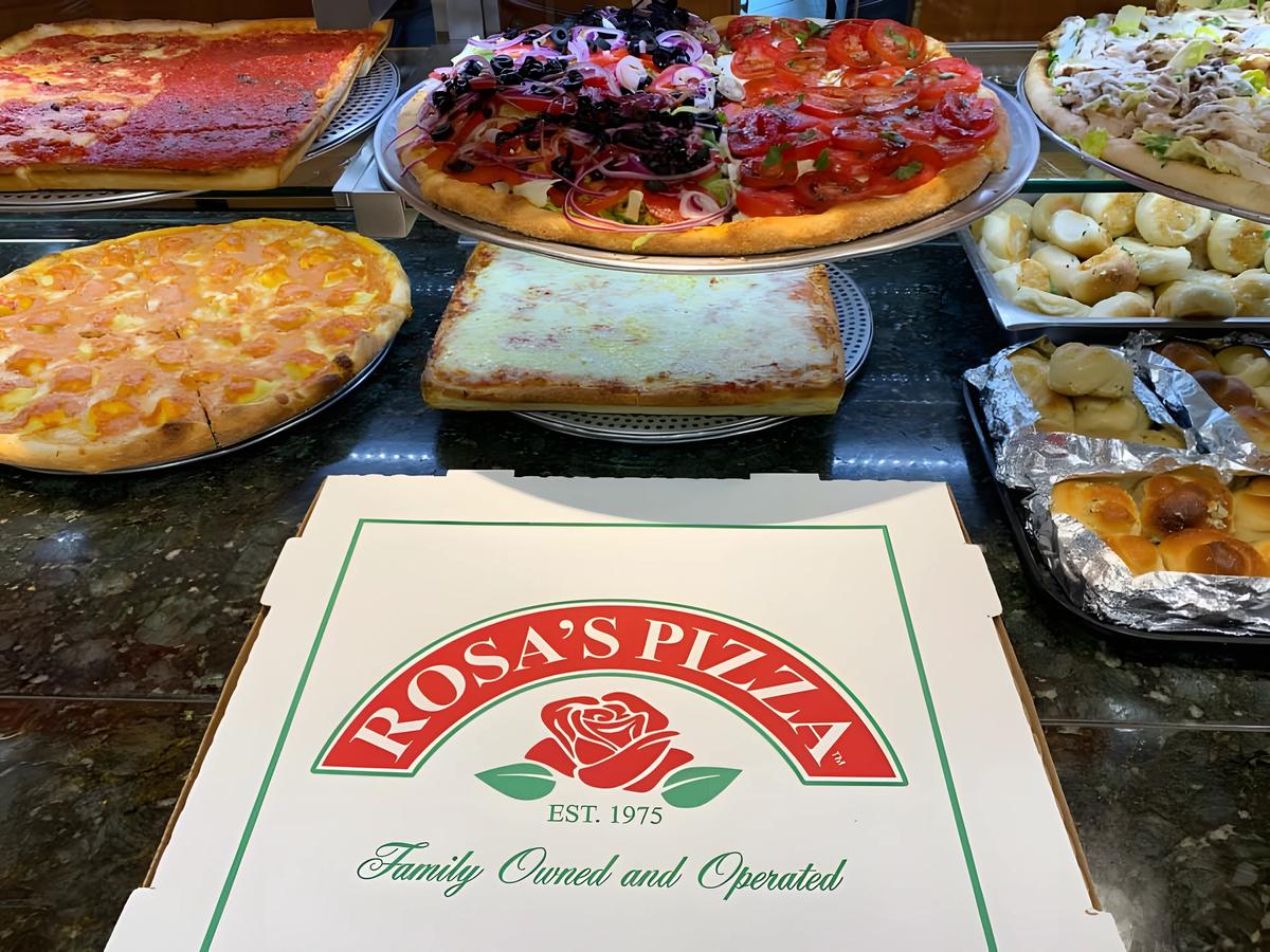 Sicilian, grandma and tomato pies with garlic knots in the Rosa's Pizza counter, a Rosa's box in front