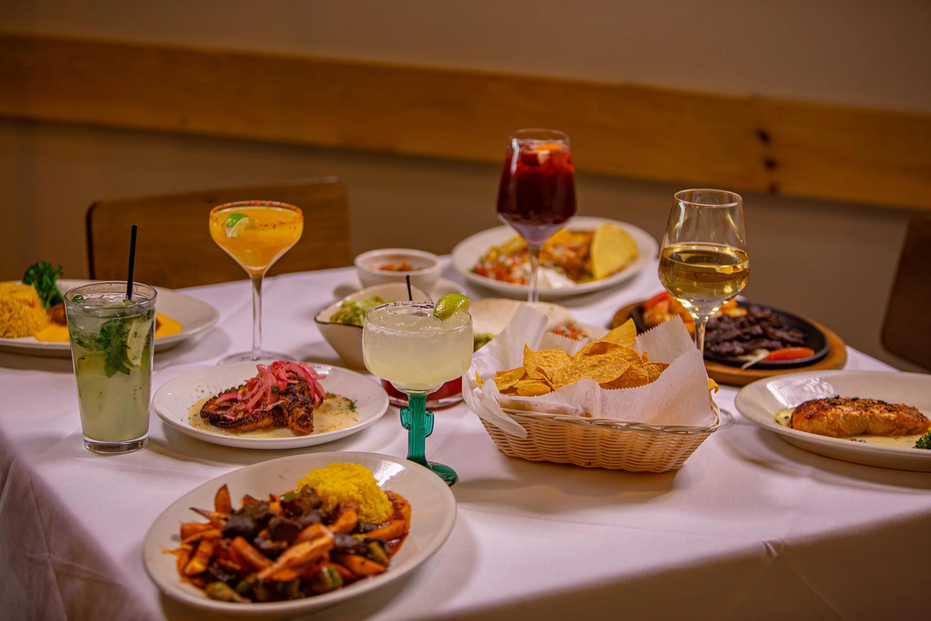 A table spread with dishes, chips and salsa, and margaritas
