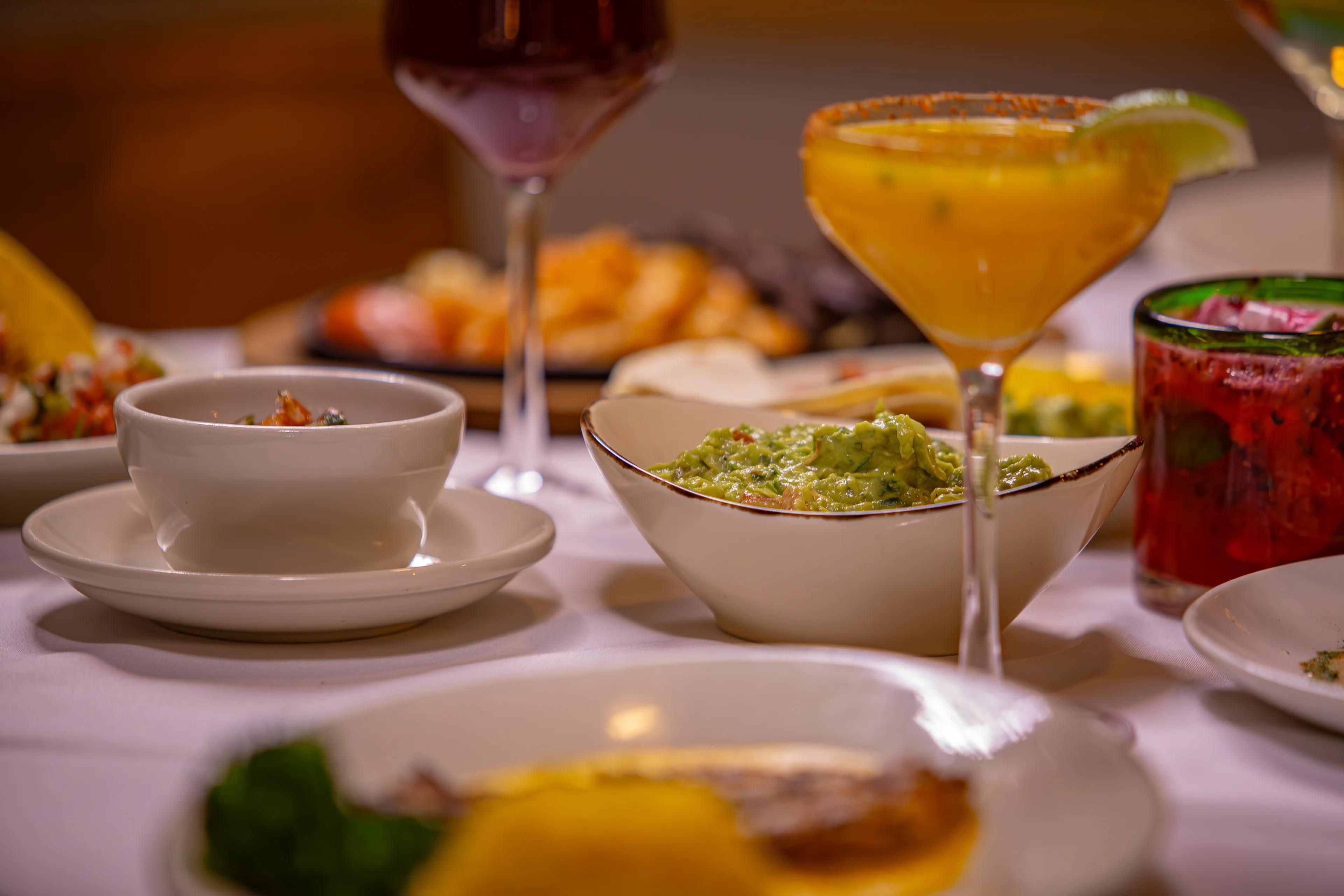 A frozen margarita with a salted rim beside plates of food