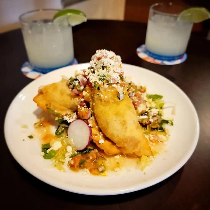 Golden fried dish topped with crumbled cheese, with margaritas behind