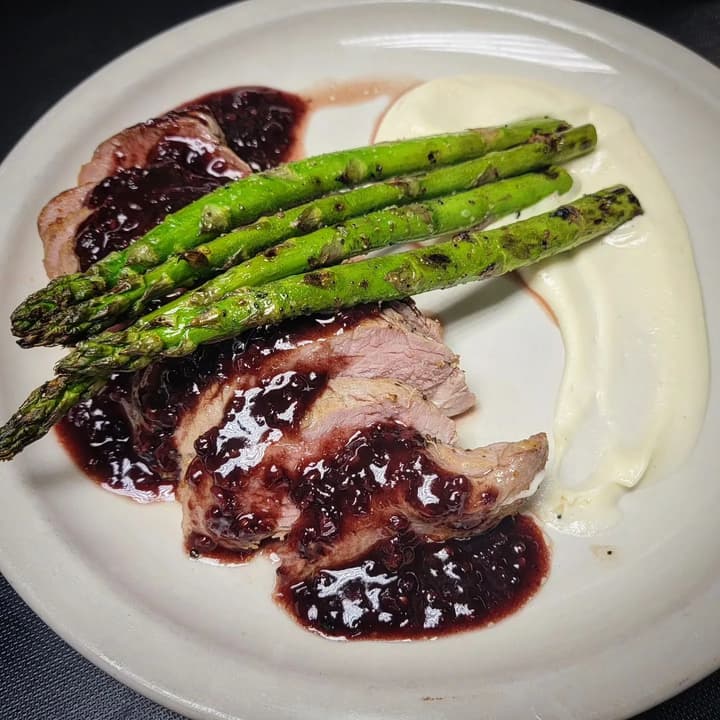 Sliced pork with a dark berry sauce and grilled asparagus