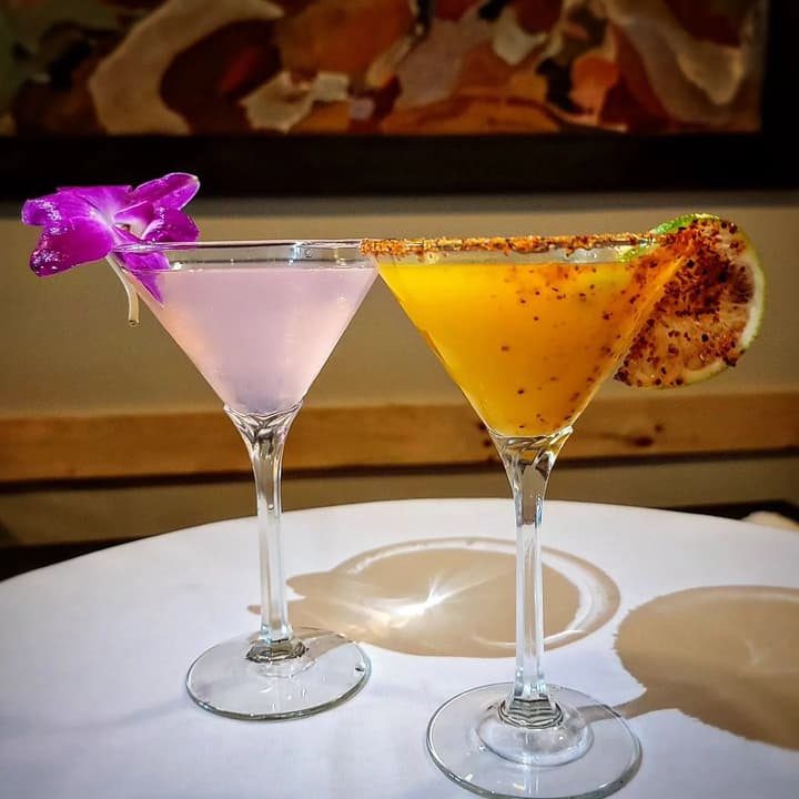 Two cocktails in martini glasses, one garnished with an orchid