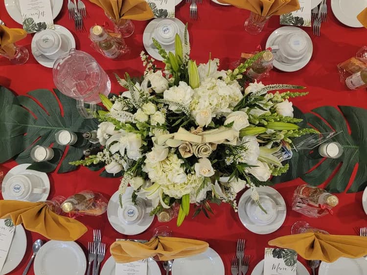 A round table set with red cloths, gold napkins and white flowers